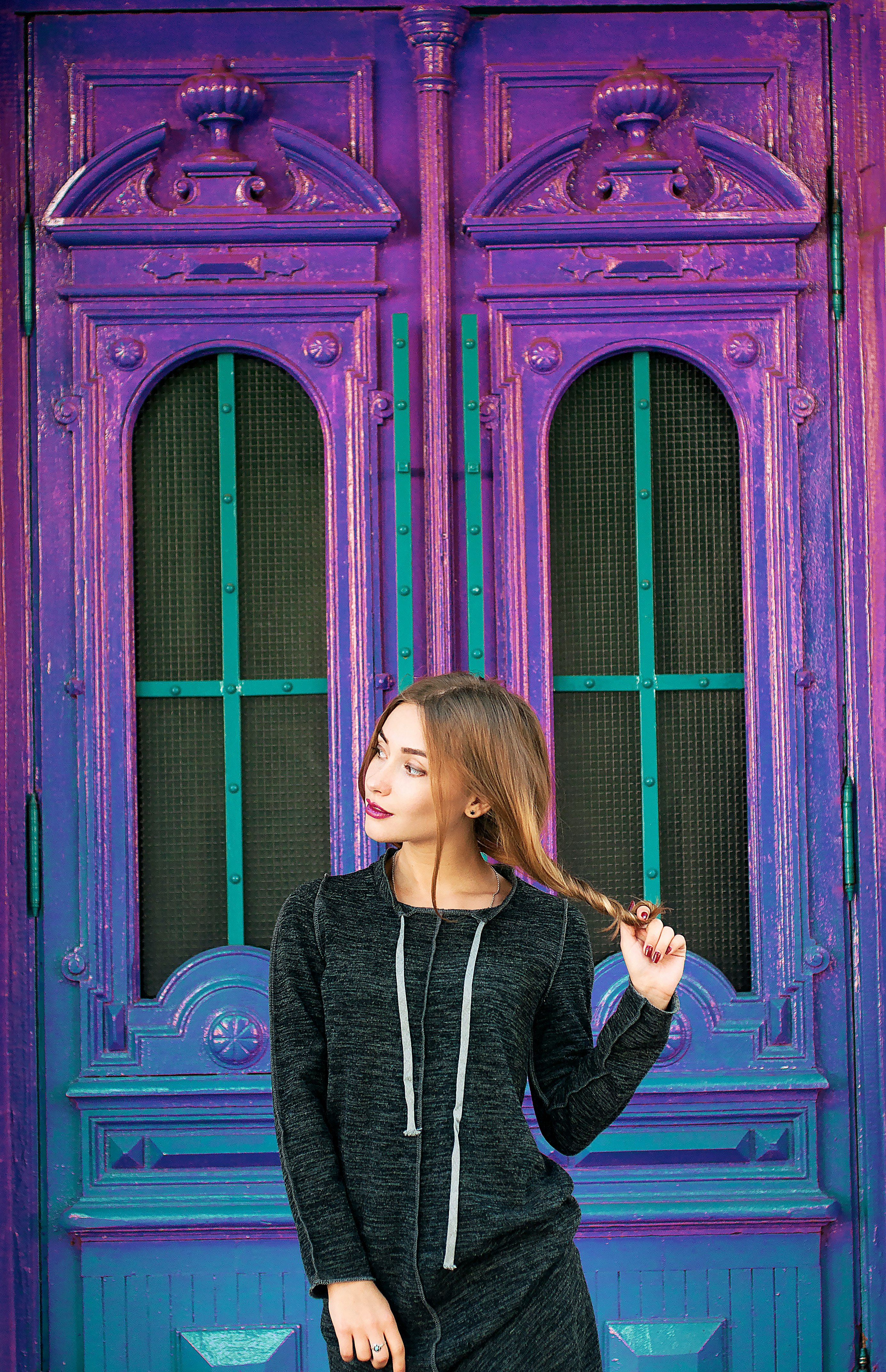 A woman holding her long hair while standing in front of a blue and purple building.